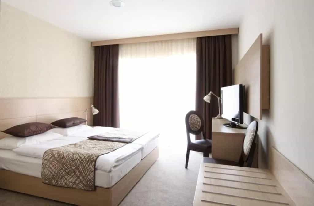 Hotel room with twin beds, desk, TV, and bright window with dark curtains, Hotel Mangart.