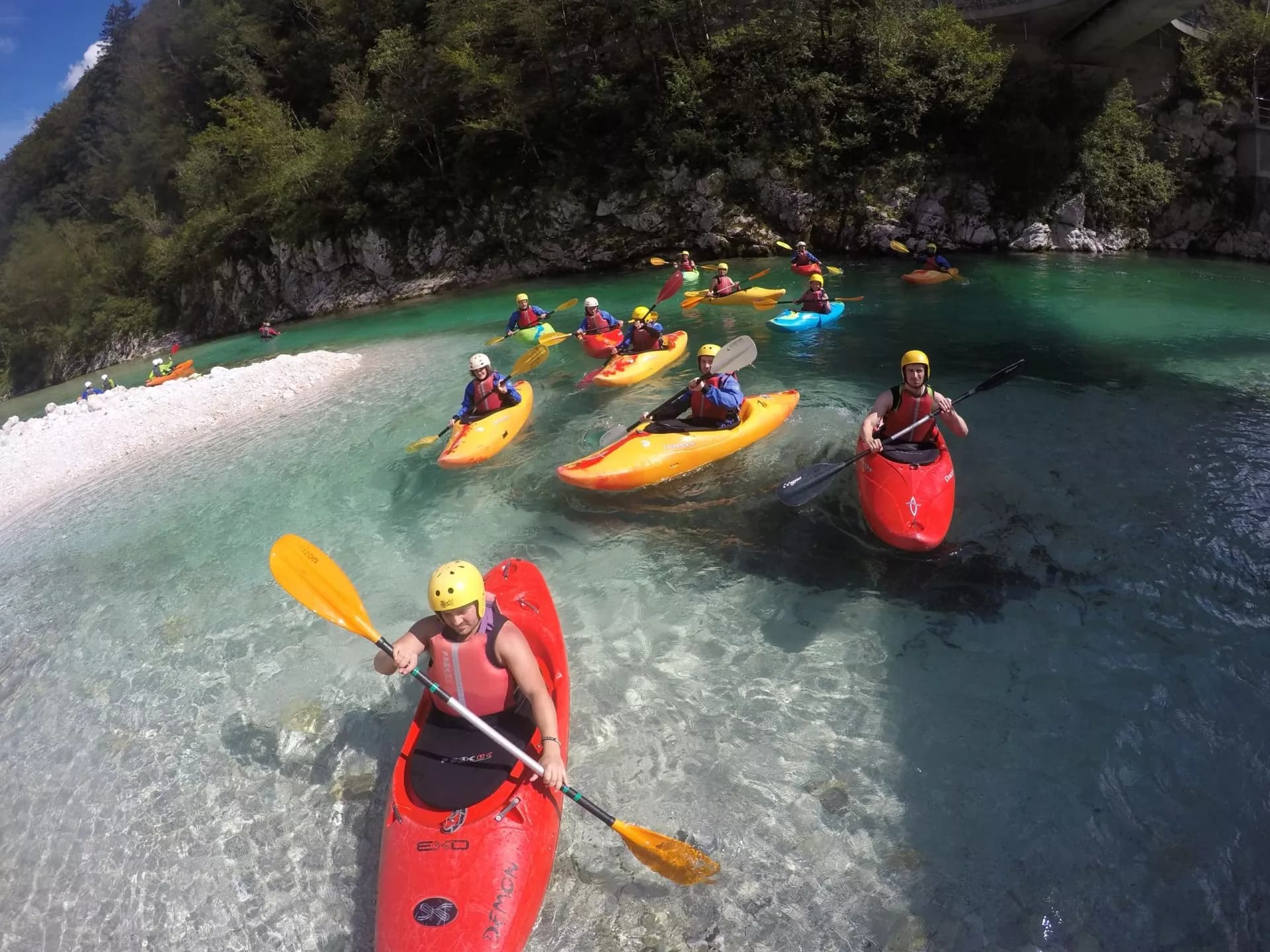 Kayaking group on clear turquoise river with forested banks in Soca Valley