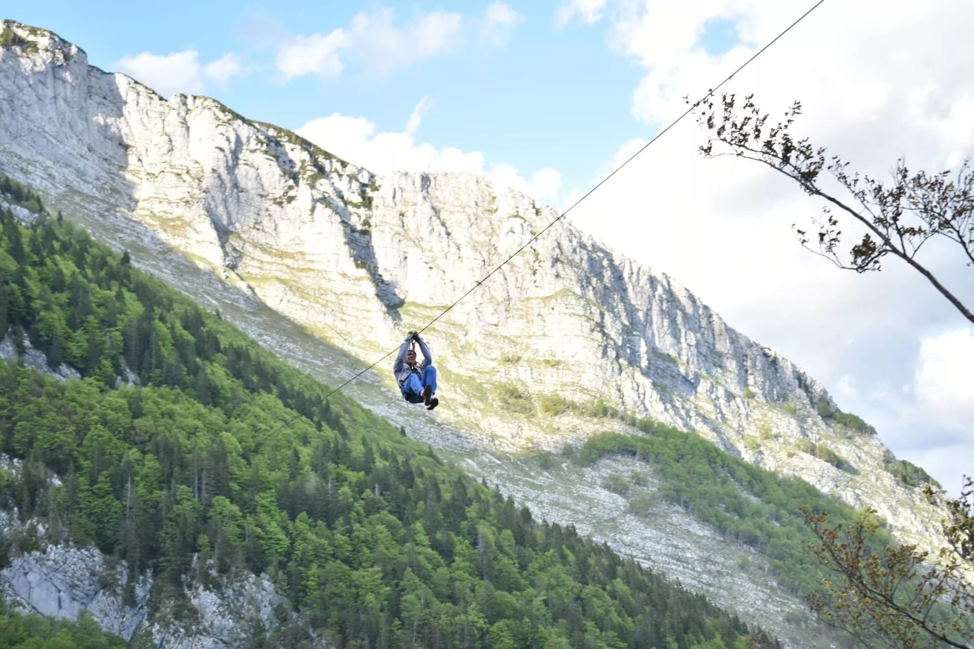 Ziplining over a lush green forested slope beneath a massive white cliff face in Bovec.