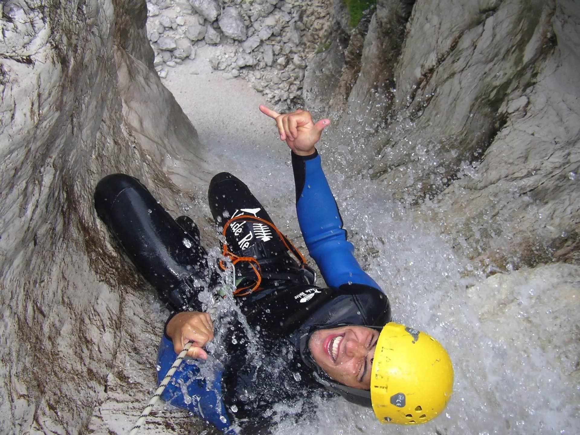 Canyoning descent down rock walls with rushing water in Slovenia, wearing a wetsuit and yellow helmet.