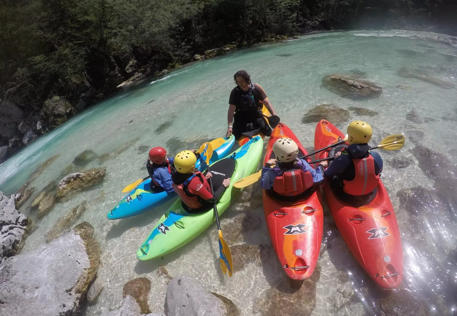 Kayaking group with instructor on clear turquoise river water surrounded by forest in Slovenia.