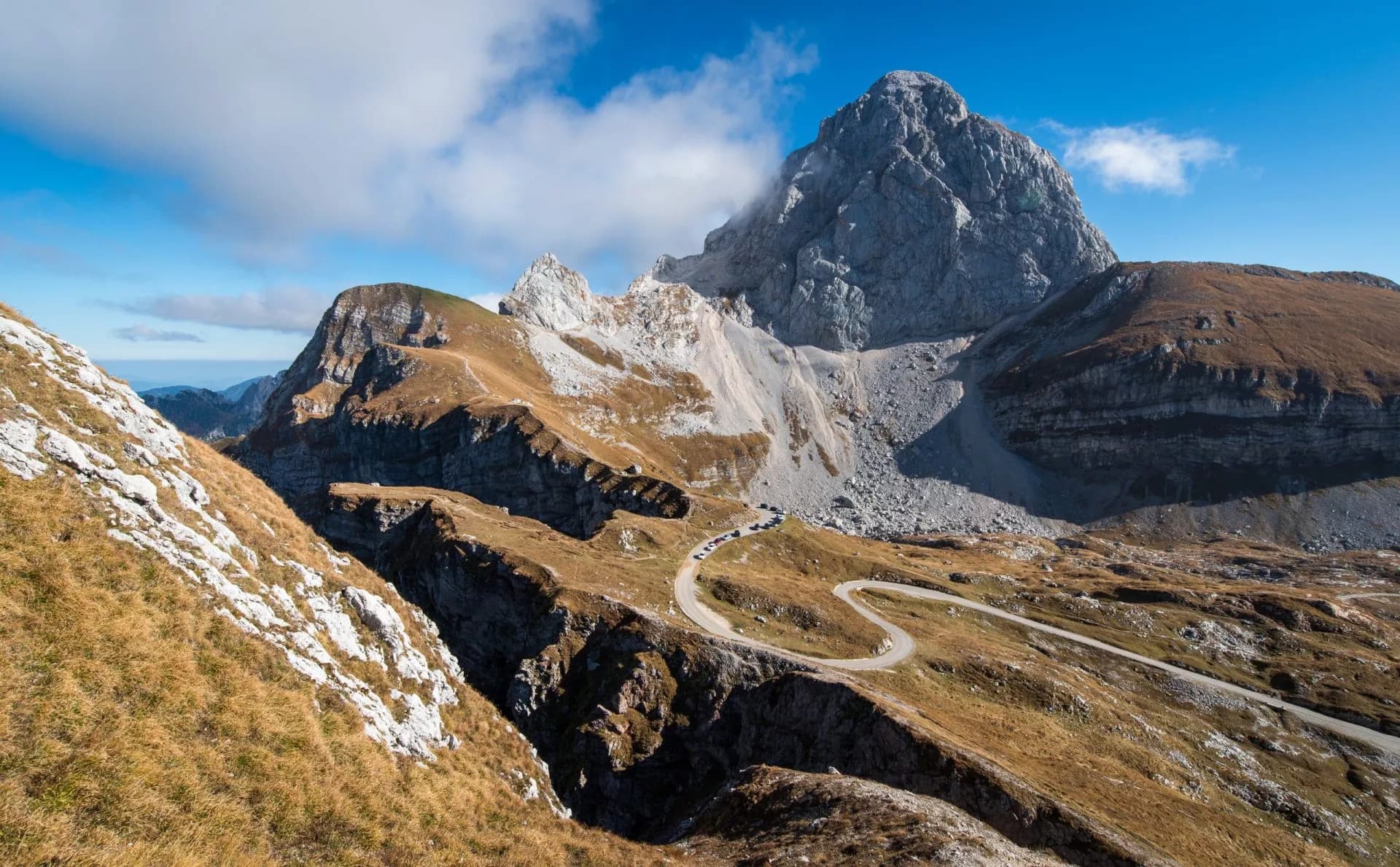 Winding mountain road scaling steep slopes below a large rocky peak, Mangart Saddle.