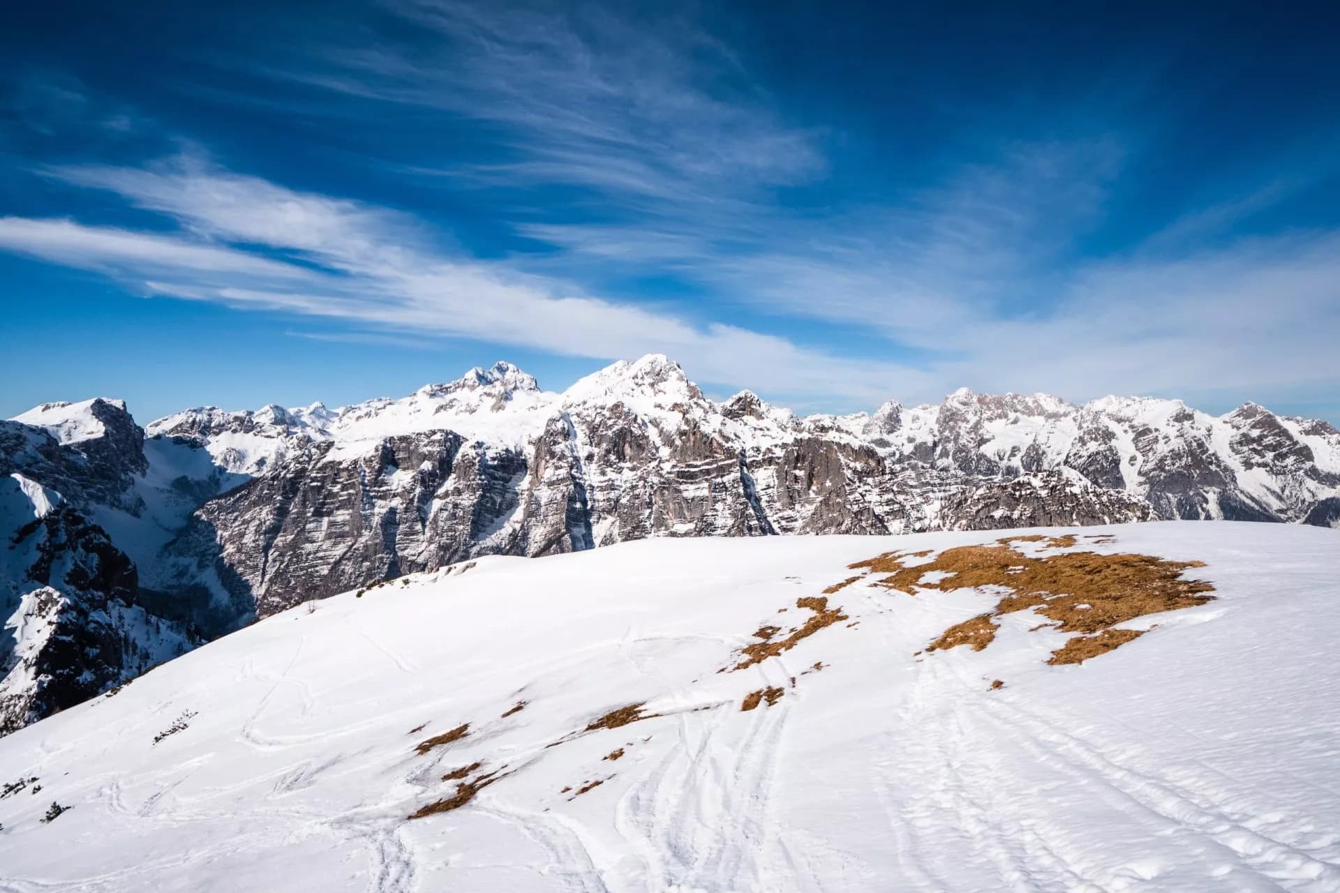 Snowy foreground leading to jagged, snow-capped Julian Alps under a bright blue sky.
