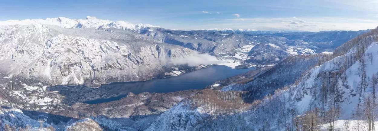 Panoramic view of Vogel overlooking Bohinj Lake surrounded by snow-covered mountains in winter.