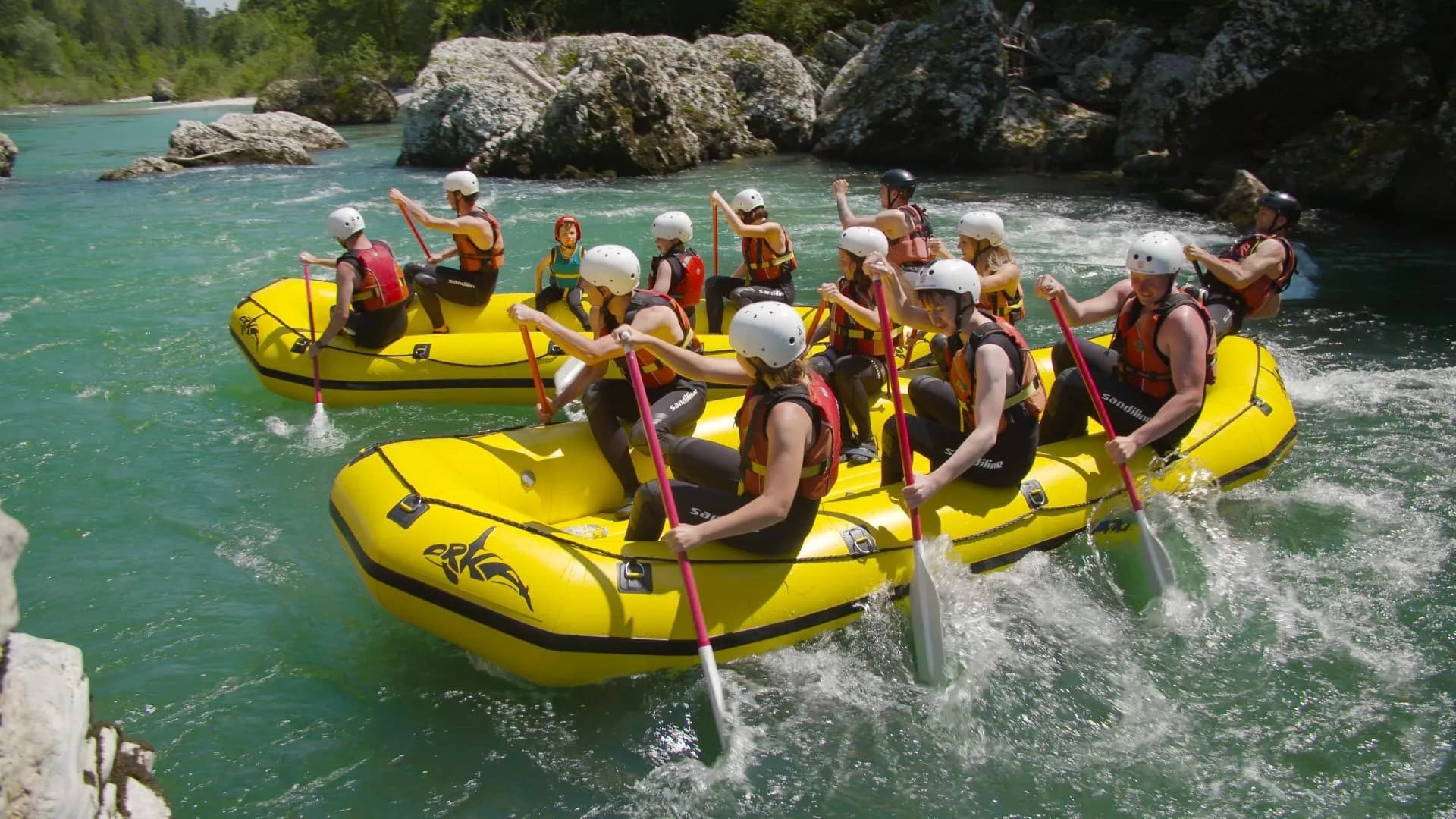 Rafting groups paddling yellow inflatable boats on turquoise river rapids in Slovenia