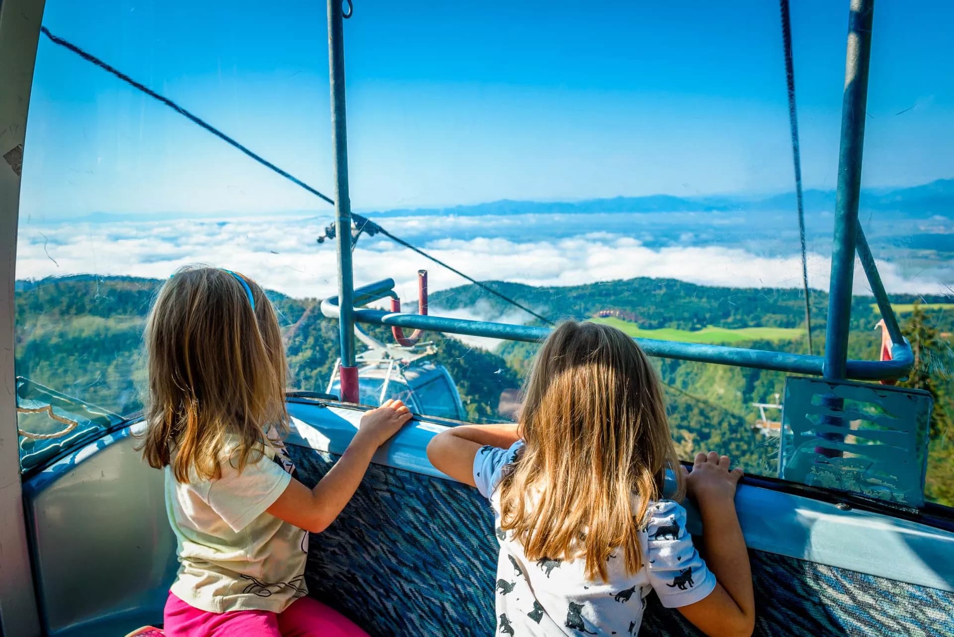Cable car ride to Krvavec with children viewing green mountains above clouds