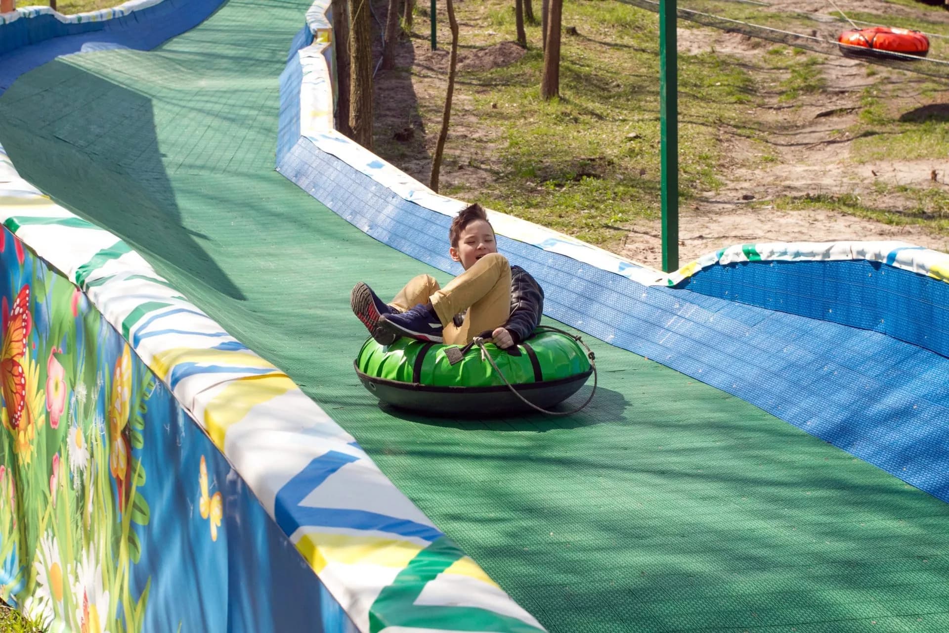 Boy tubing down a green artificial slide with colorful barriers at Krvavec.