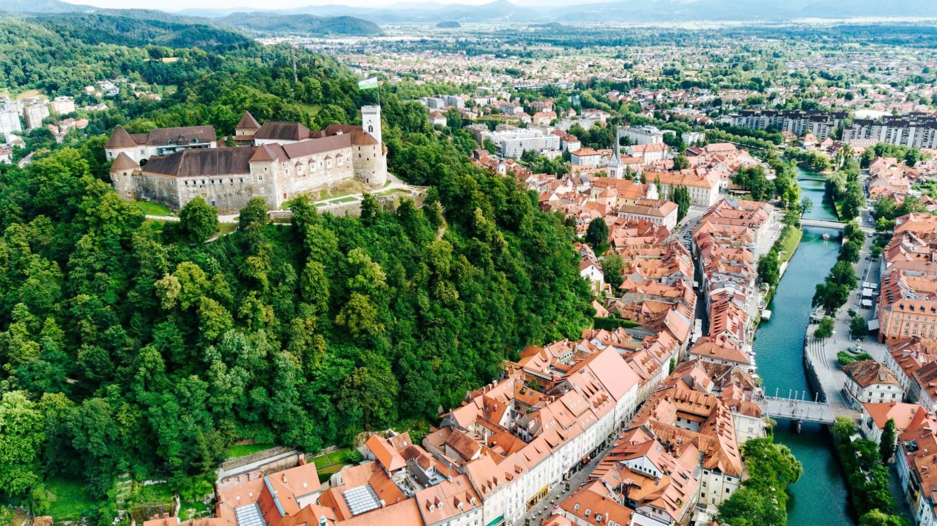 Aerial view of Ljubljana Castle above green hill overlooking city and Ljubljanica River.