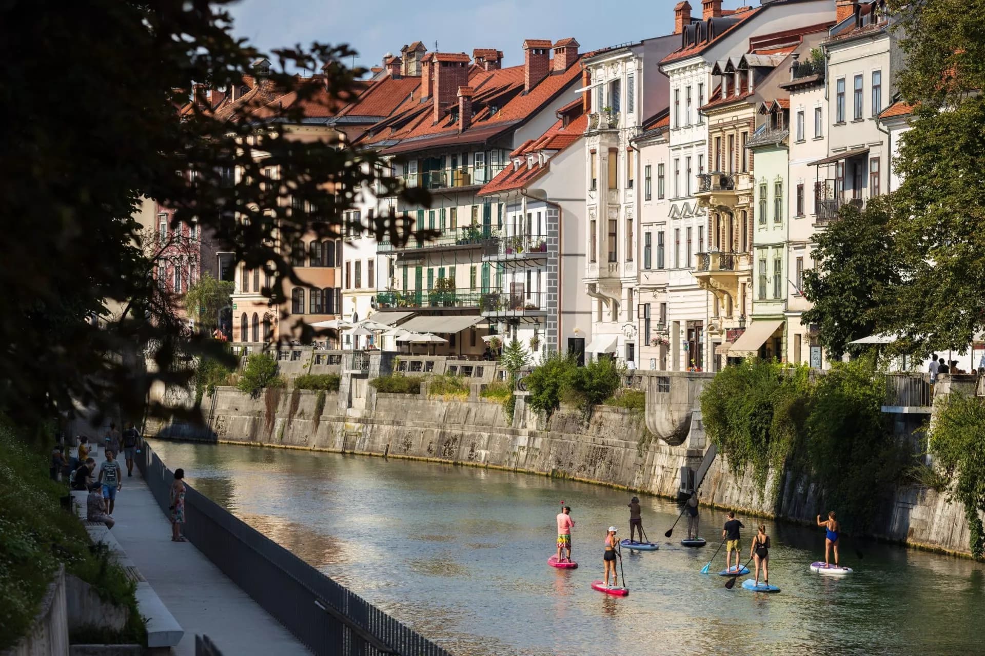 Stand-up paddleboarding on river past historic buildings in Ljubljana Old Town.