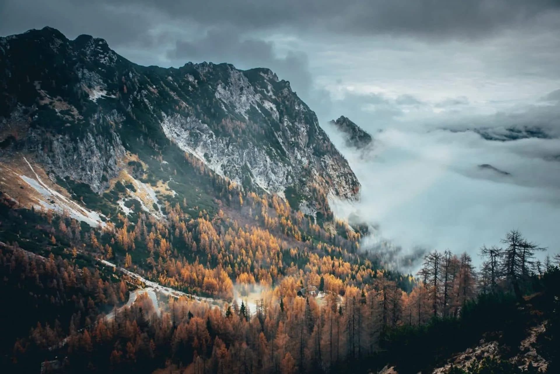 Mountain pass road winding through autumn forest below rocky peaks shrouded in fog in Slovenia.