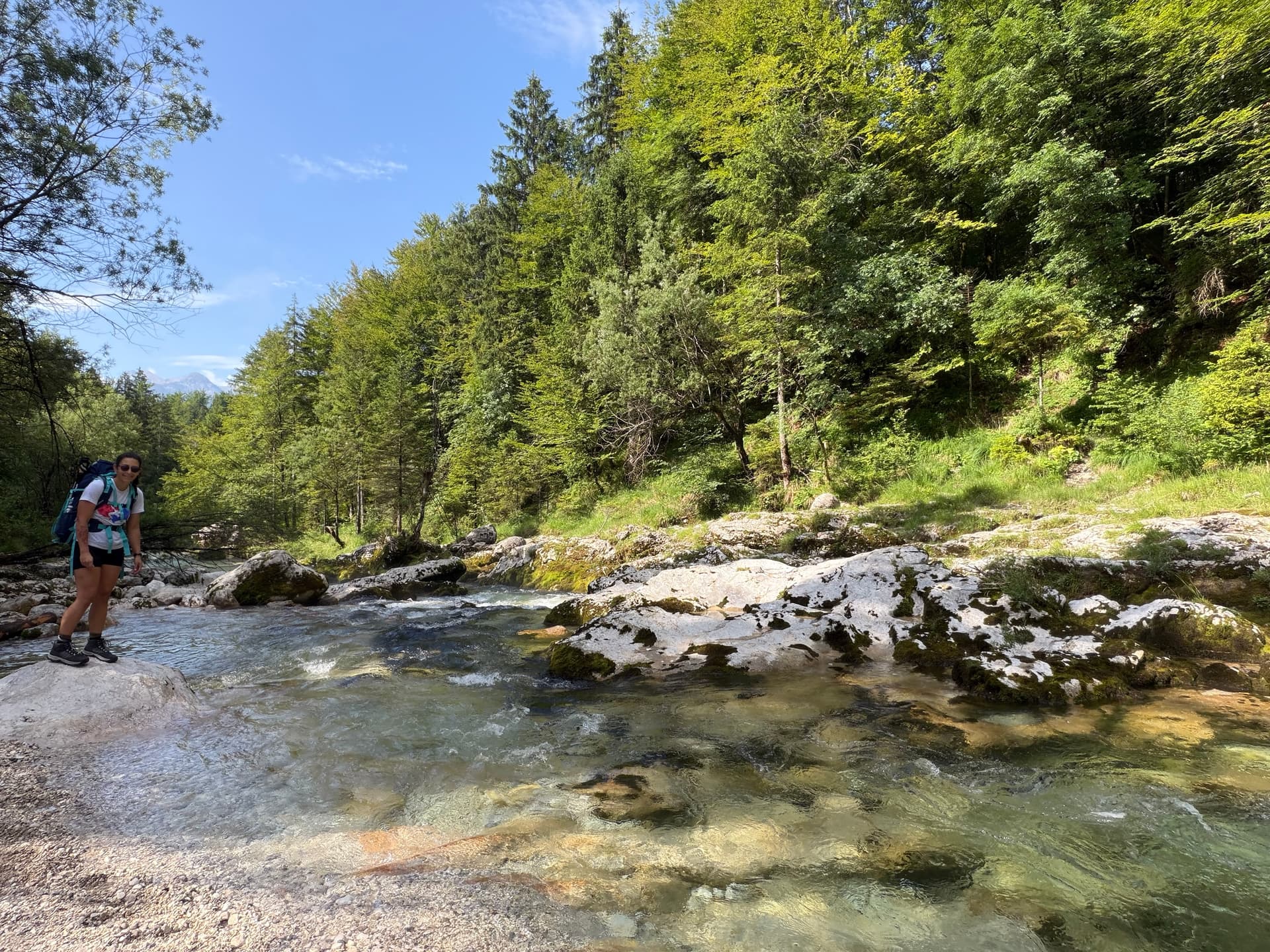 Hiker with backpack standing by clear river over pale rocks in forest
