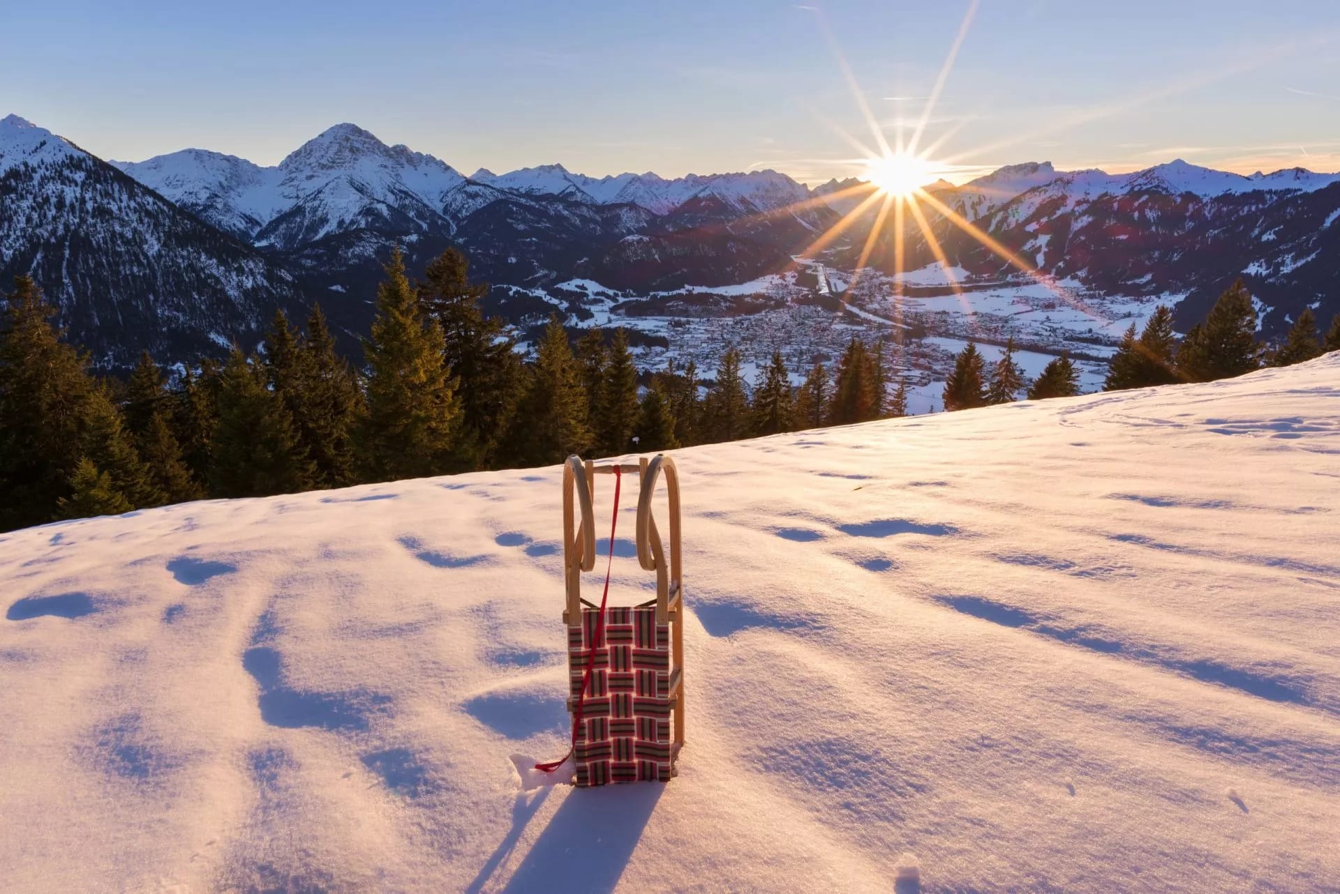 Wooden sled on snow with sunset over snowy mountains and a valley town in Slovenia.