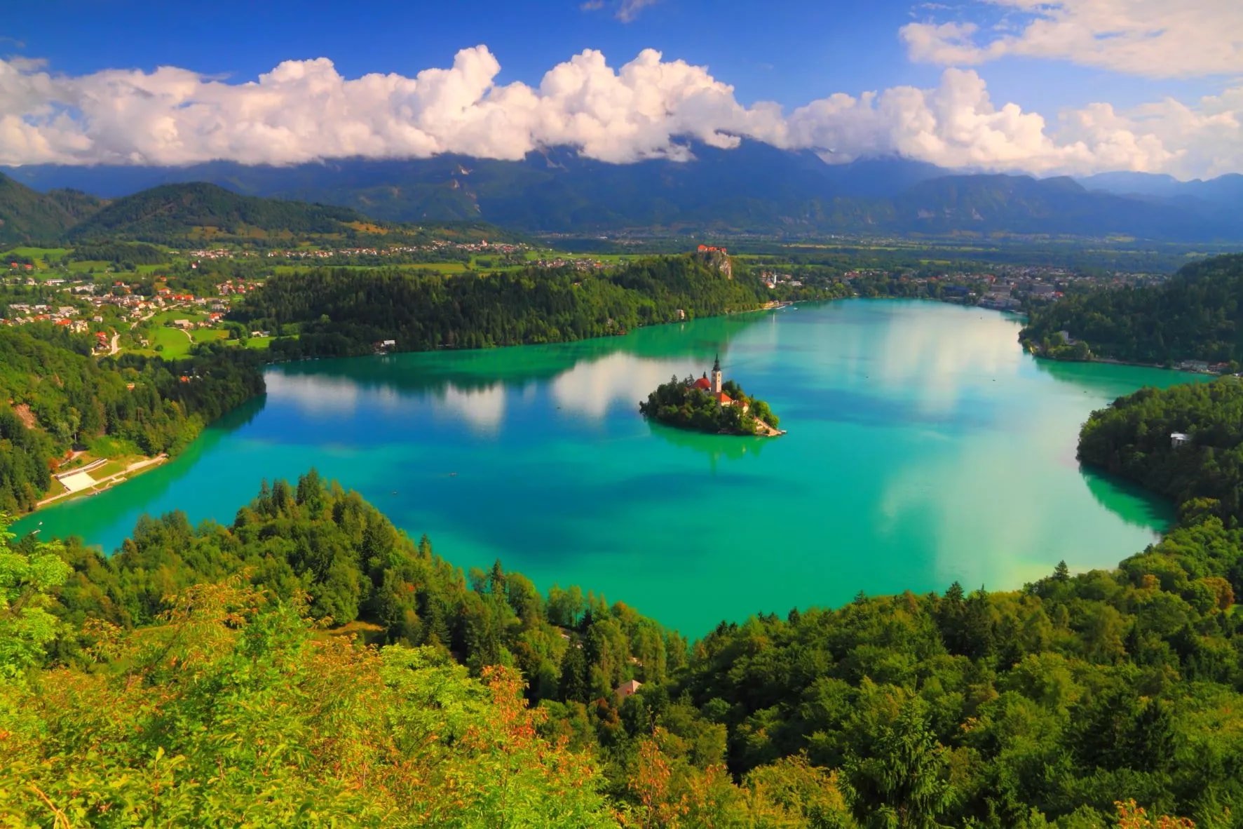Lake Bled island church surrounded by turquoise water, lush forests, and Julian Alps mountains.