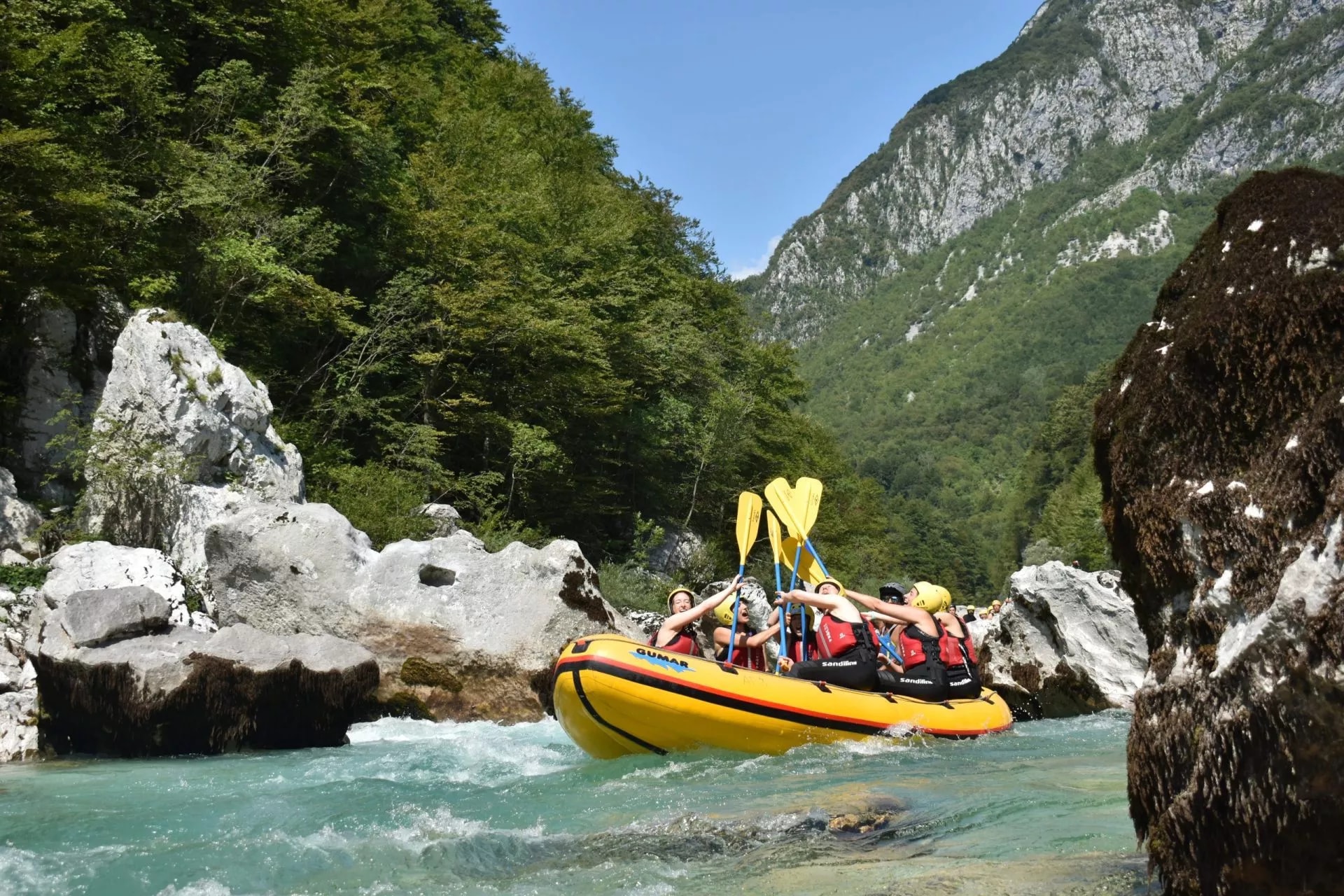 White-water rafting on turquoise river through a gorge with steep, forested mountains.