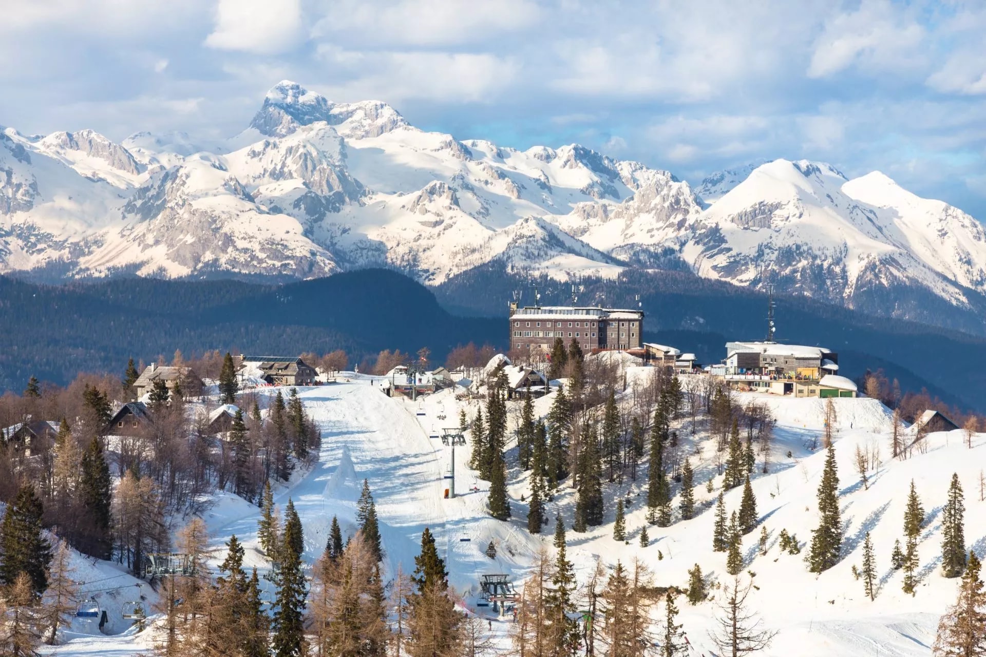 Ski resort with lodge buildings below massive snow-covered Mount Triglav in winter.