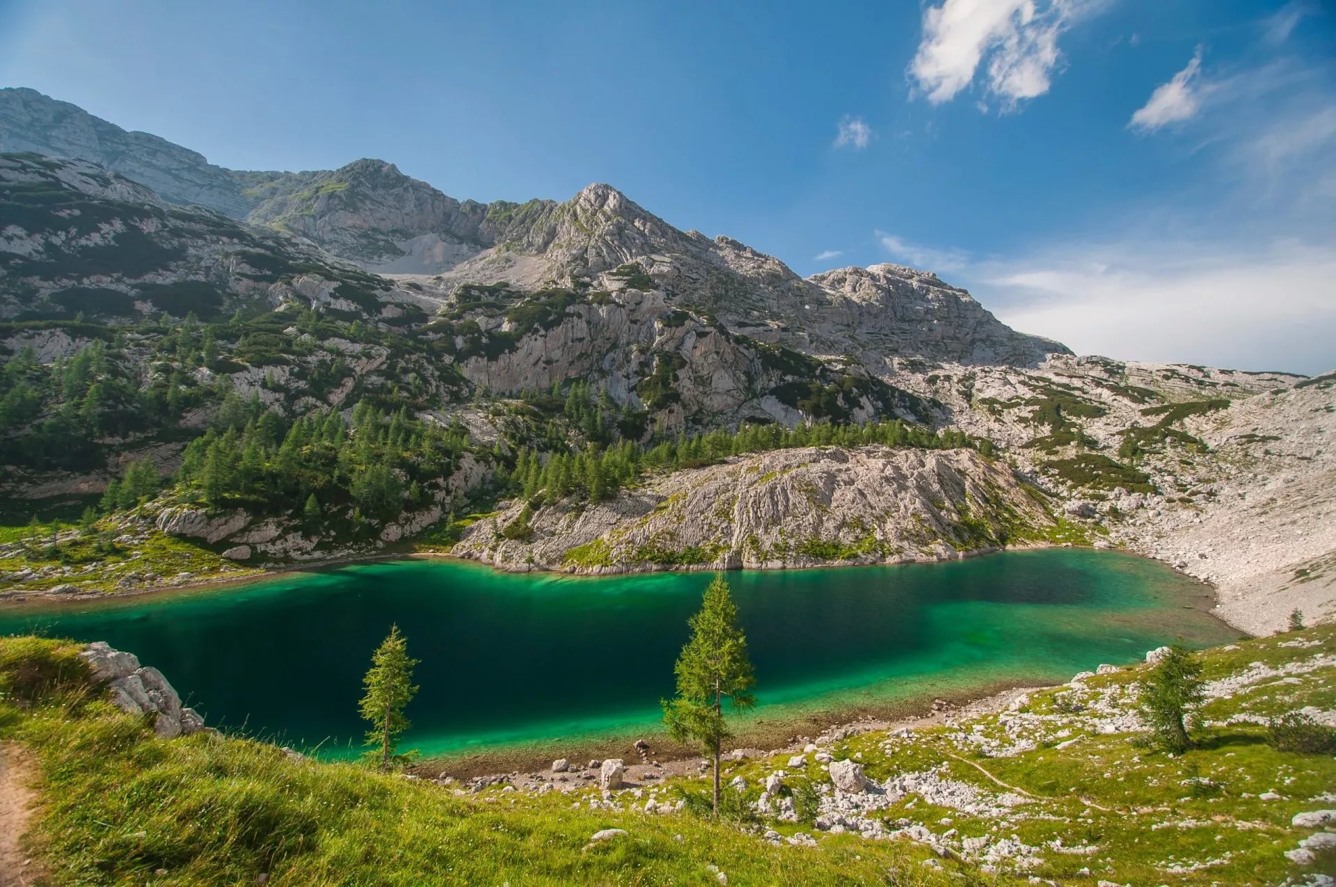 Alpine lake with emerald water surrounded by rocky mountains and green vegetation under blue sky.