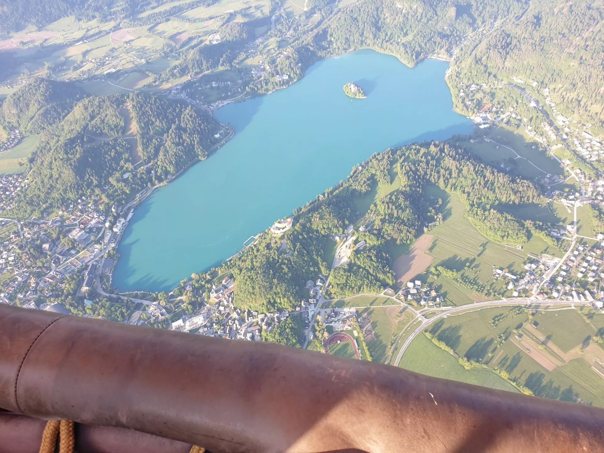 Aerial view of Lake Bled with island church, town, and surrounding green hills.