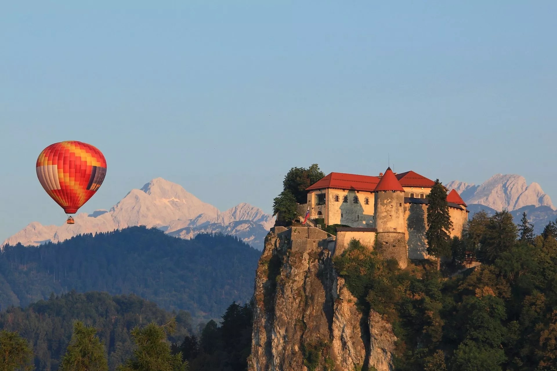 Hot air balloon flying near Bled Castle with snowy mountains in the background