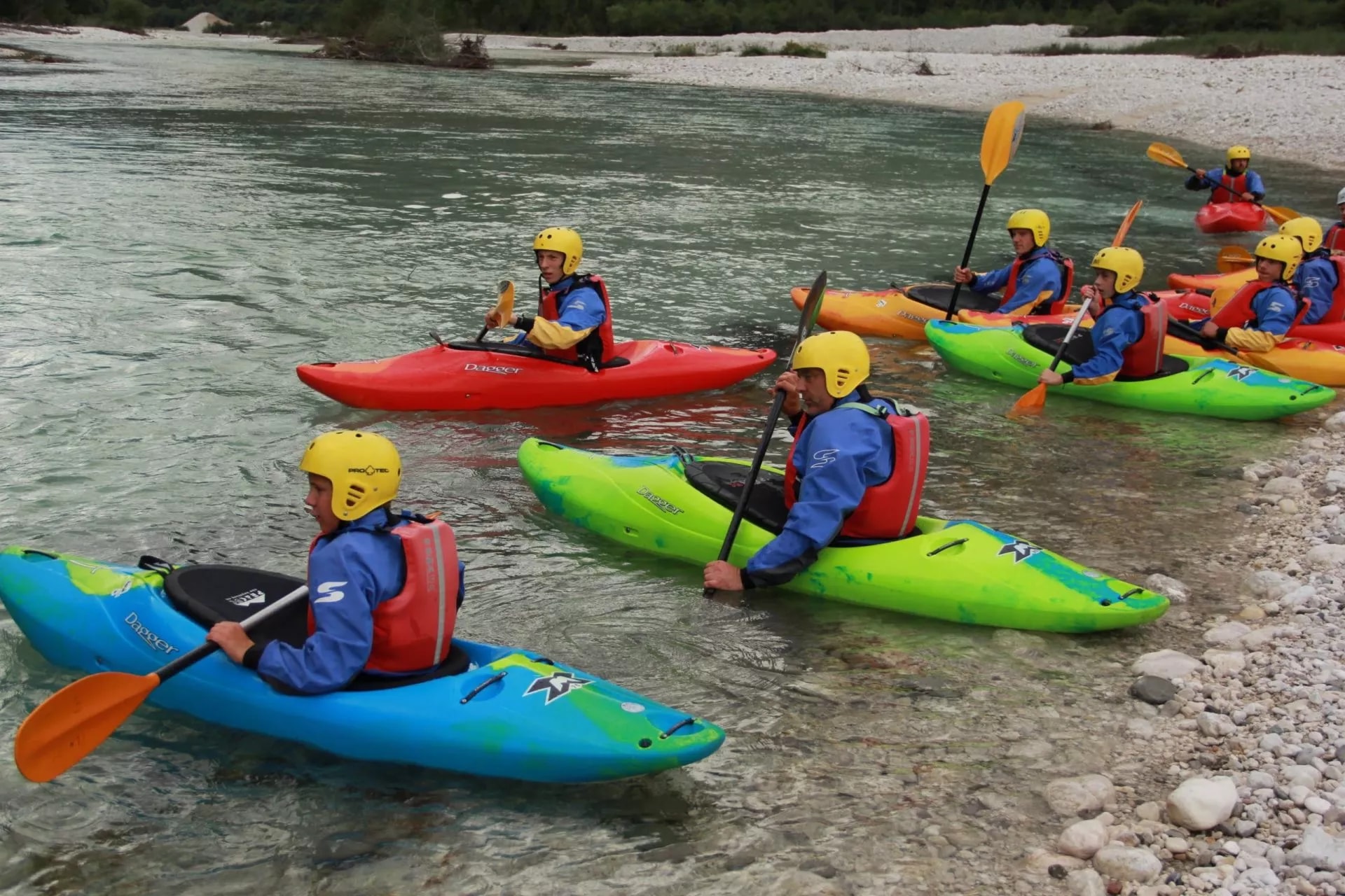 Kayaking group on clear river near rocky shore, using colorful kayaks in Slovenia.