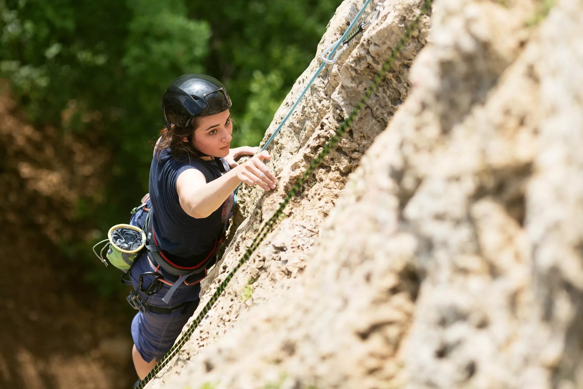 Rock climber ascending a sunlit crag with green trees in the background in Slovenia.