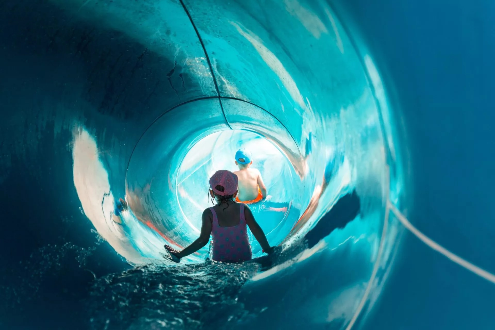 Children sliding down a bright blue enclosed water slide with rushing water.