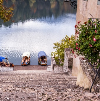 Stone steps leading down to a lake shore with two small wooden boats docked near autumn foliage.