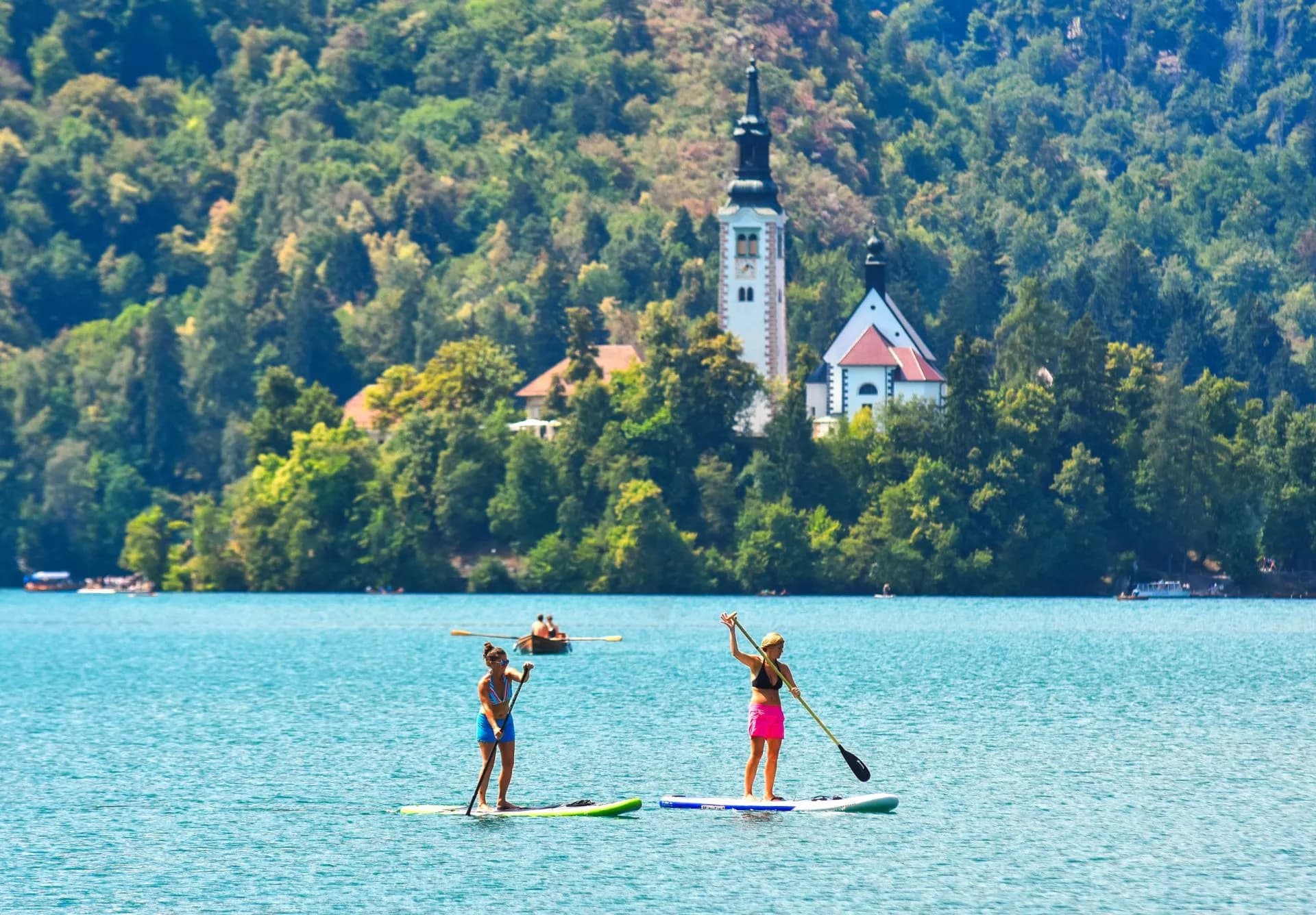 Paddleboarding on Lake Bled with the island church visible on the forested shore.