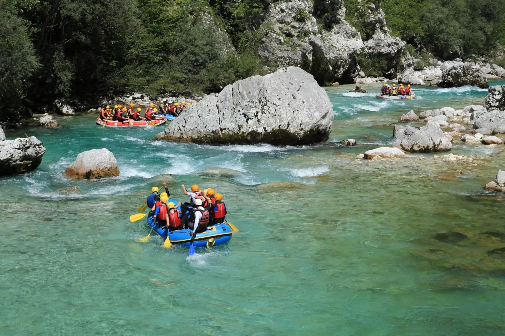 Rafting on clear turquoise Soca River Valley rapids surrounded by large boulders and green forest.