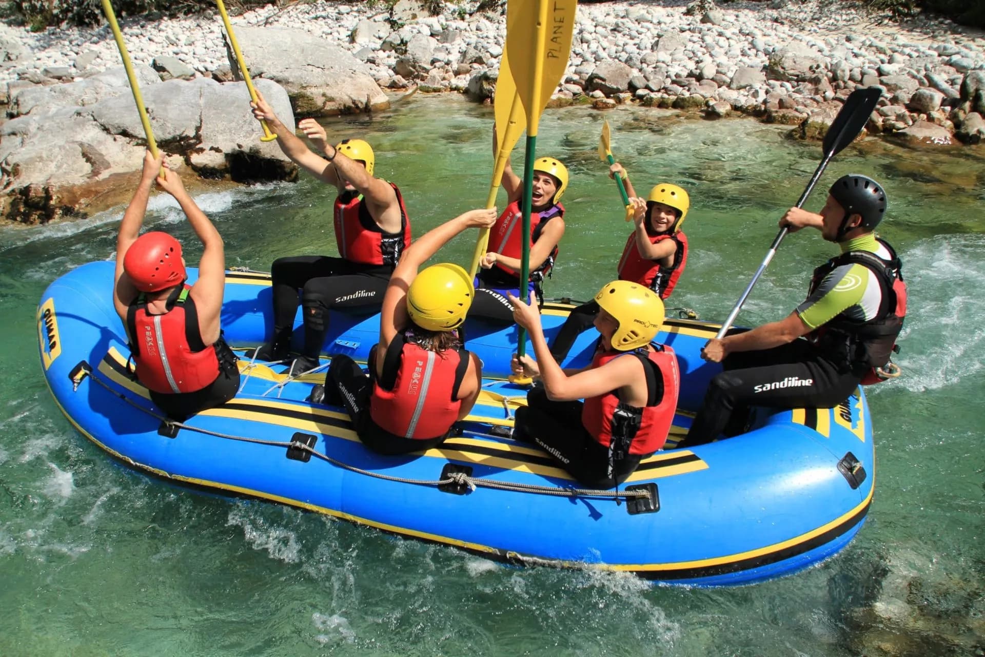 White-water rafting group paddling blue raft down rocky river with clear green water