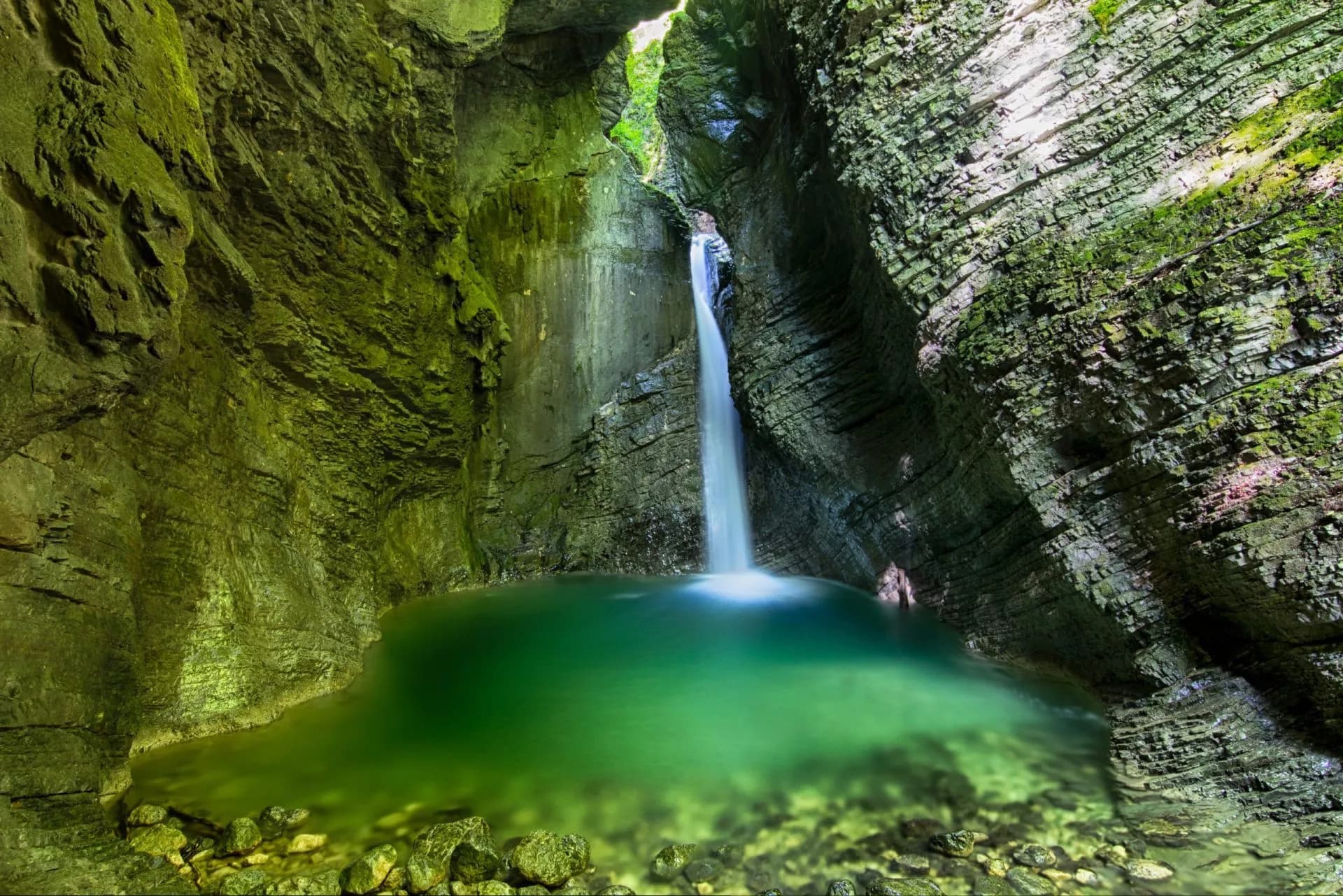 Waterfall plunging into a green pool inside a narrow, moss-covered rock gorge, Kozjak.
