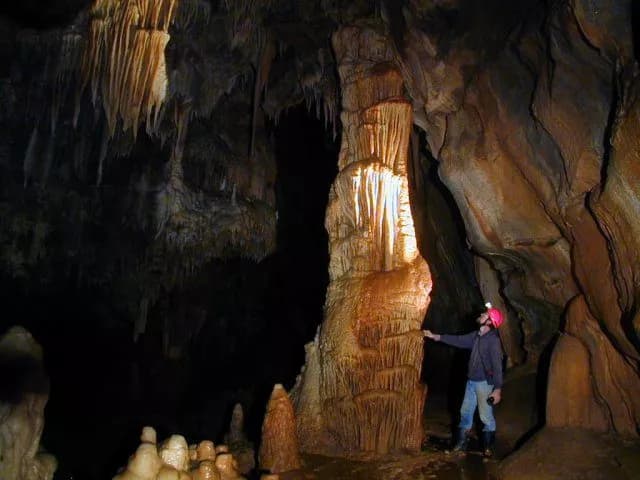 Caver exploring large stalagmite formation illuminated inside Planina cave.