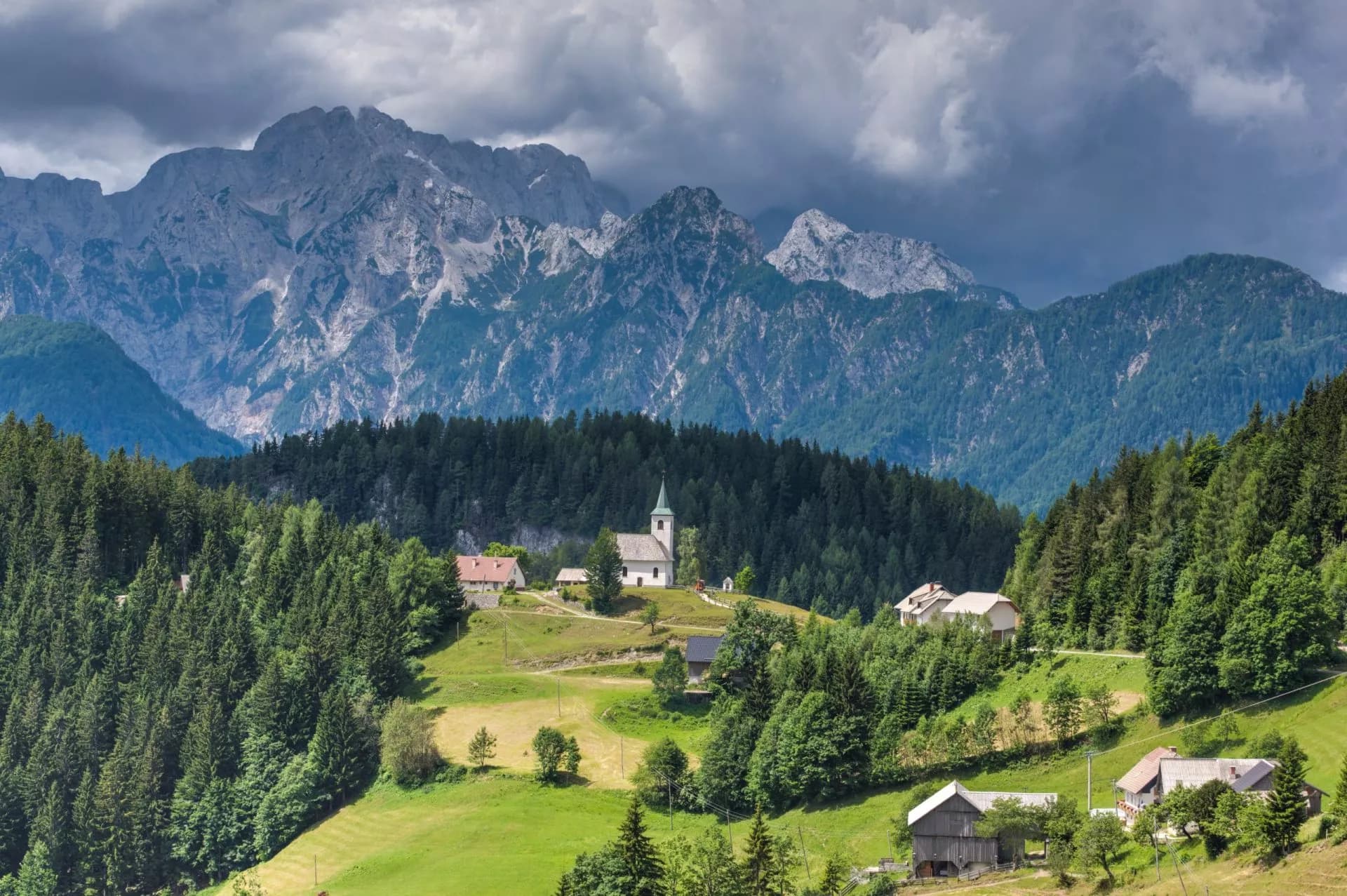 Panoramic view of Logar Valley with church, houses, green meadows, and rugged mountains under cloudy sky.