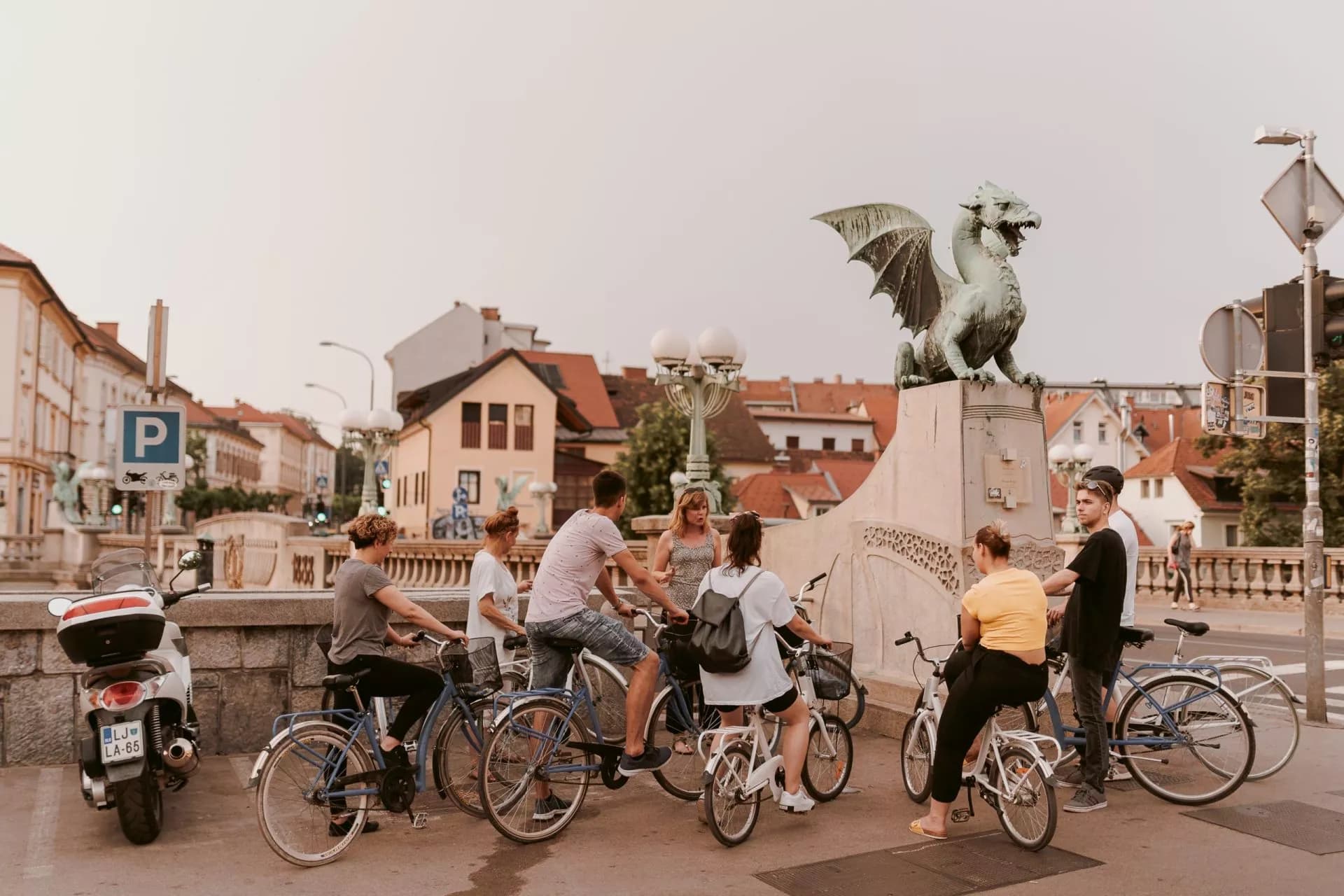 Cyclists gathered near the Dragon Bridge statue with a scooter parked nearby in Ljubljana.