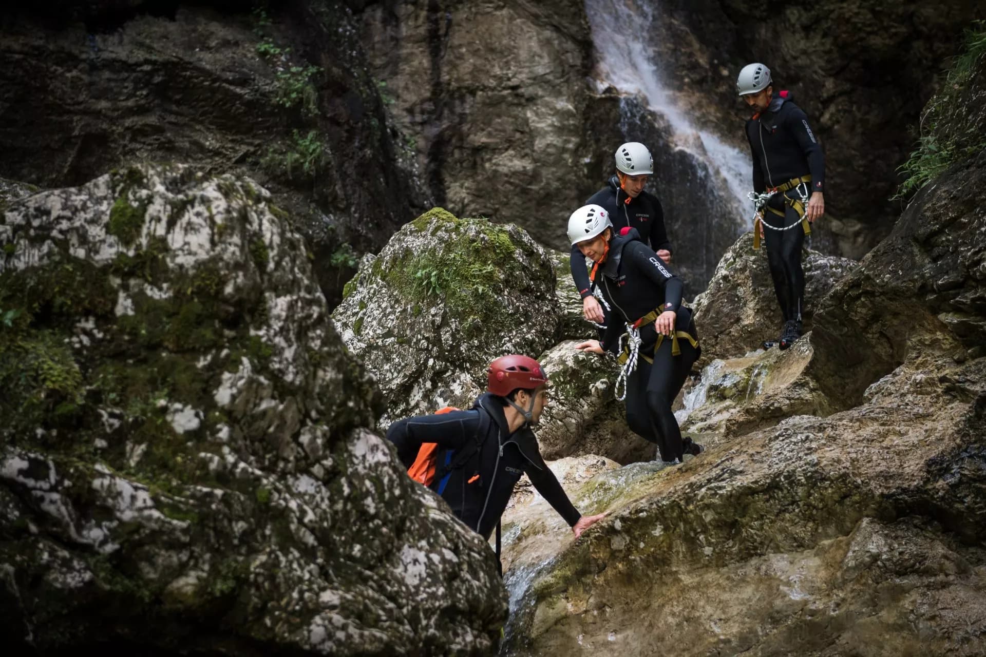 Canyoning group climbing wet rocks near a waterfall in Slovenia.
