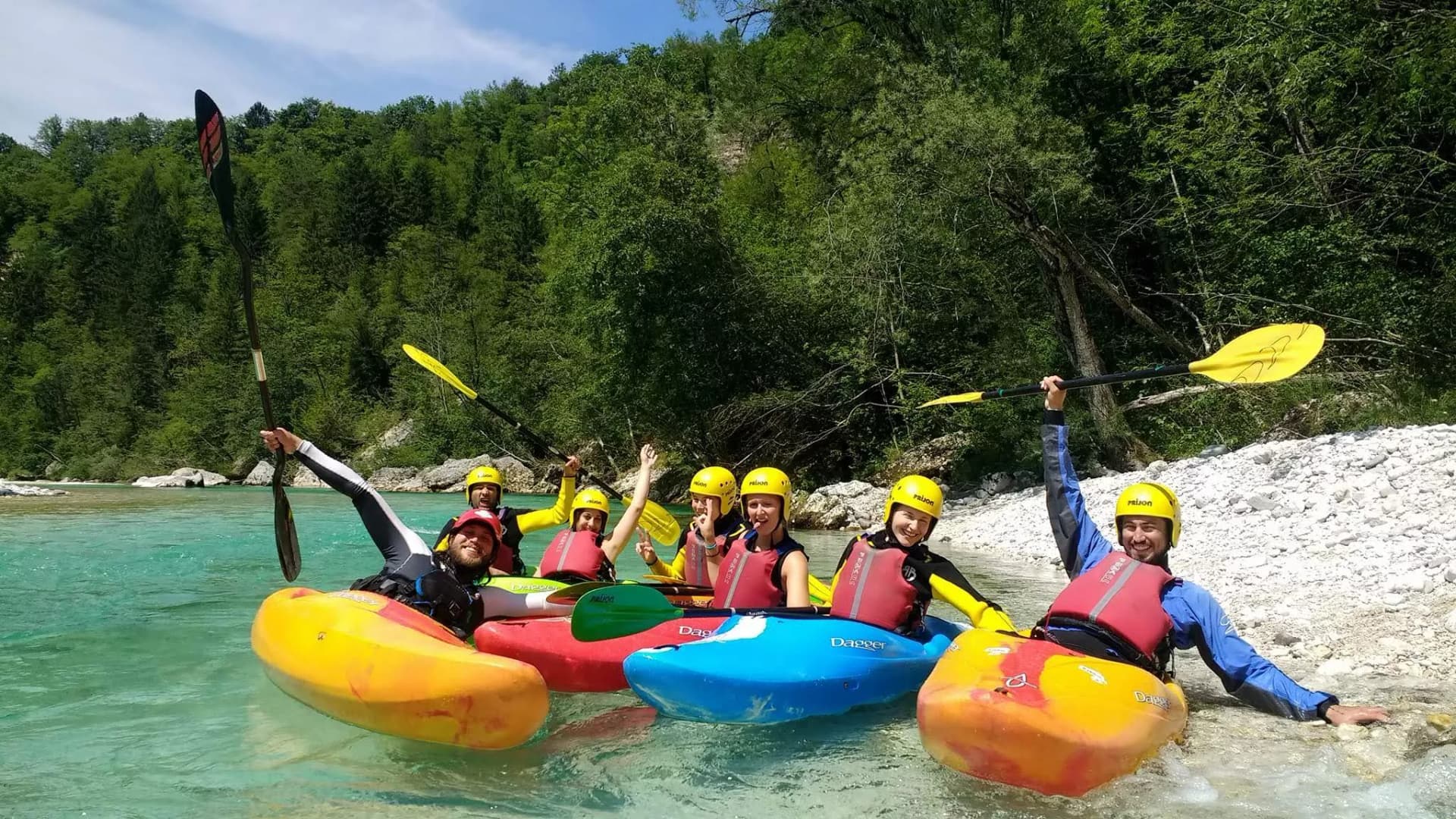 Kayaking group with yellow helmets on turquoise river near rocky shore in Slovenia