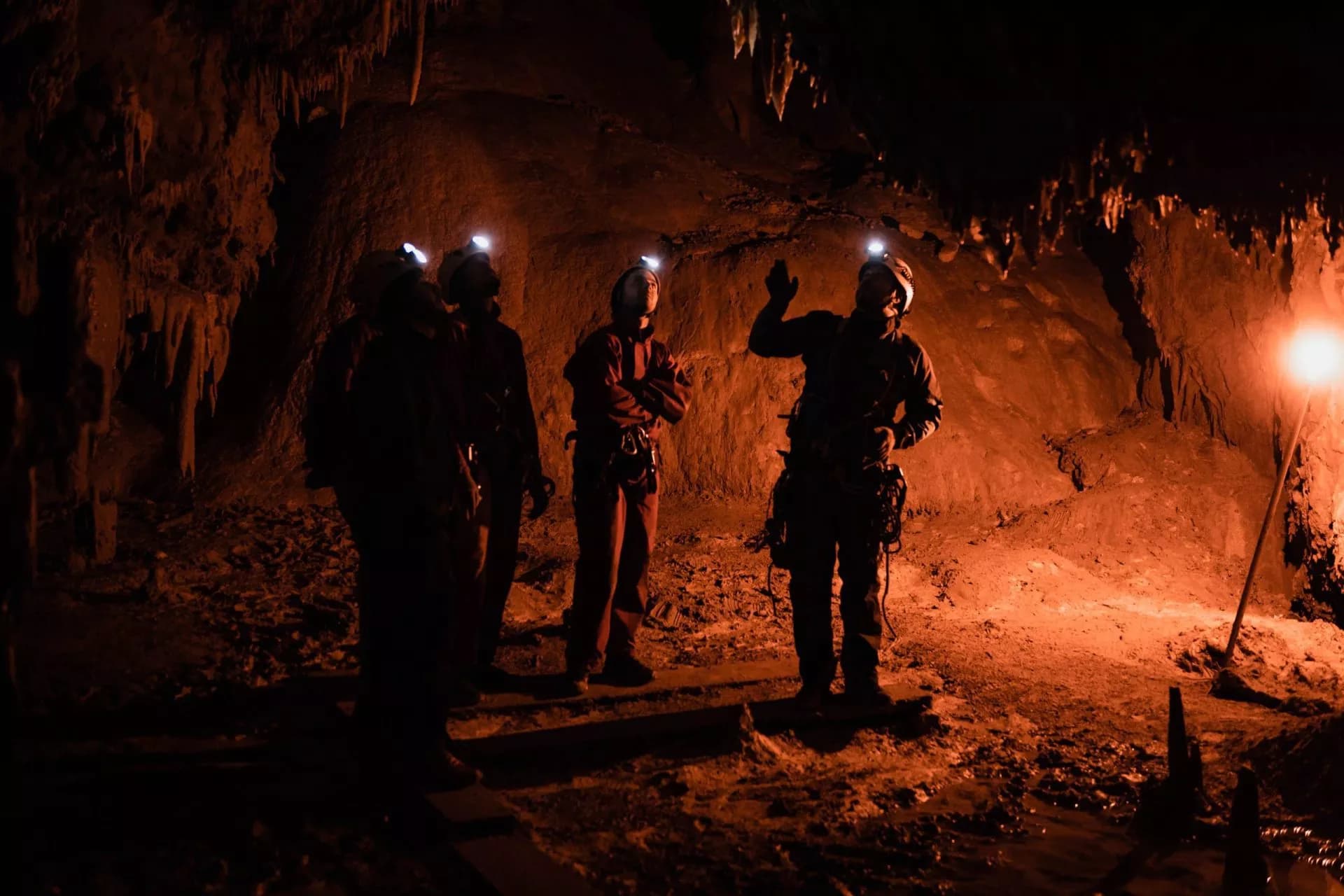 Cavers with headlamps exploring a dark cave with orange lighting near Bled.