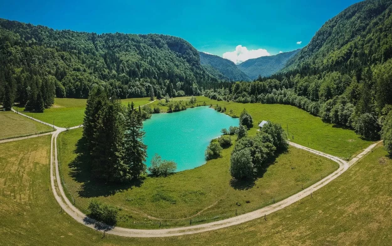 Turquoise mountain lake surrounded by green forests and fields under a bright blue sky at Lake Kreda.