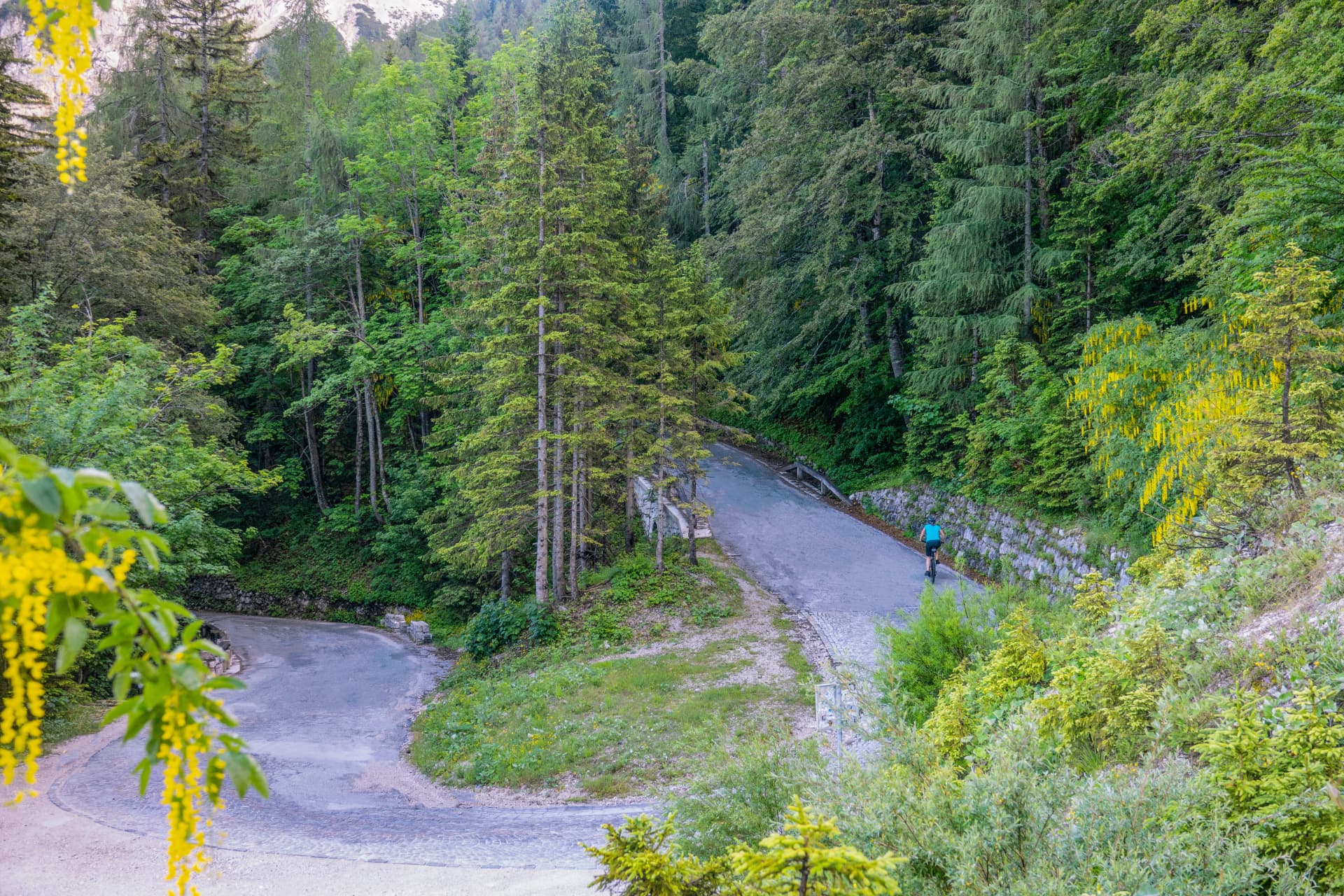 AERIAL: Unrecognizable woman rides a mountain bike up an empty mountain pass
