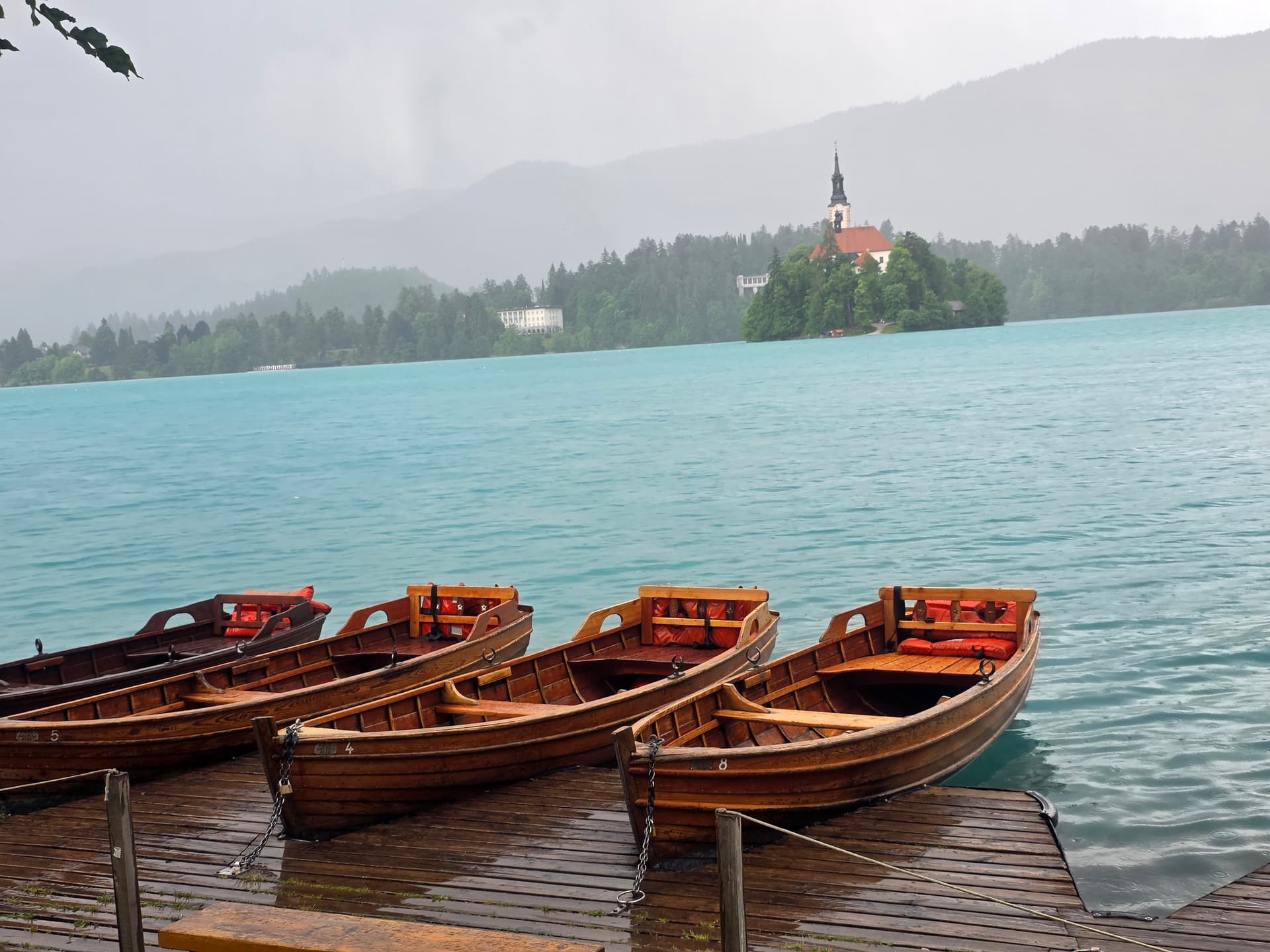 Traditional wooden Pletna boats moored on a wooden dock at Lake Bled with the island church in the background