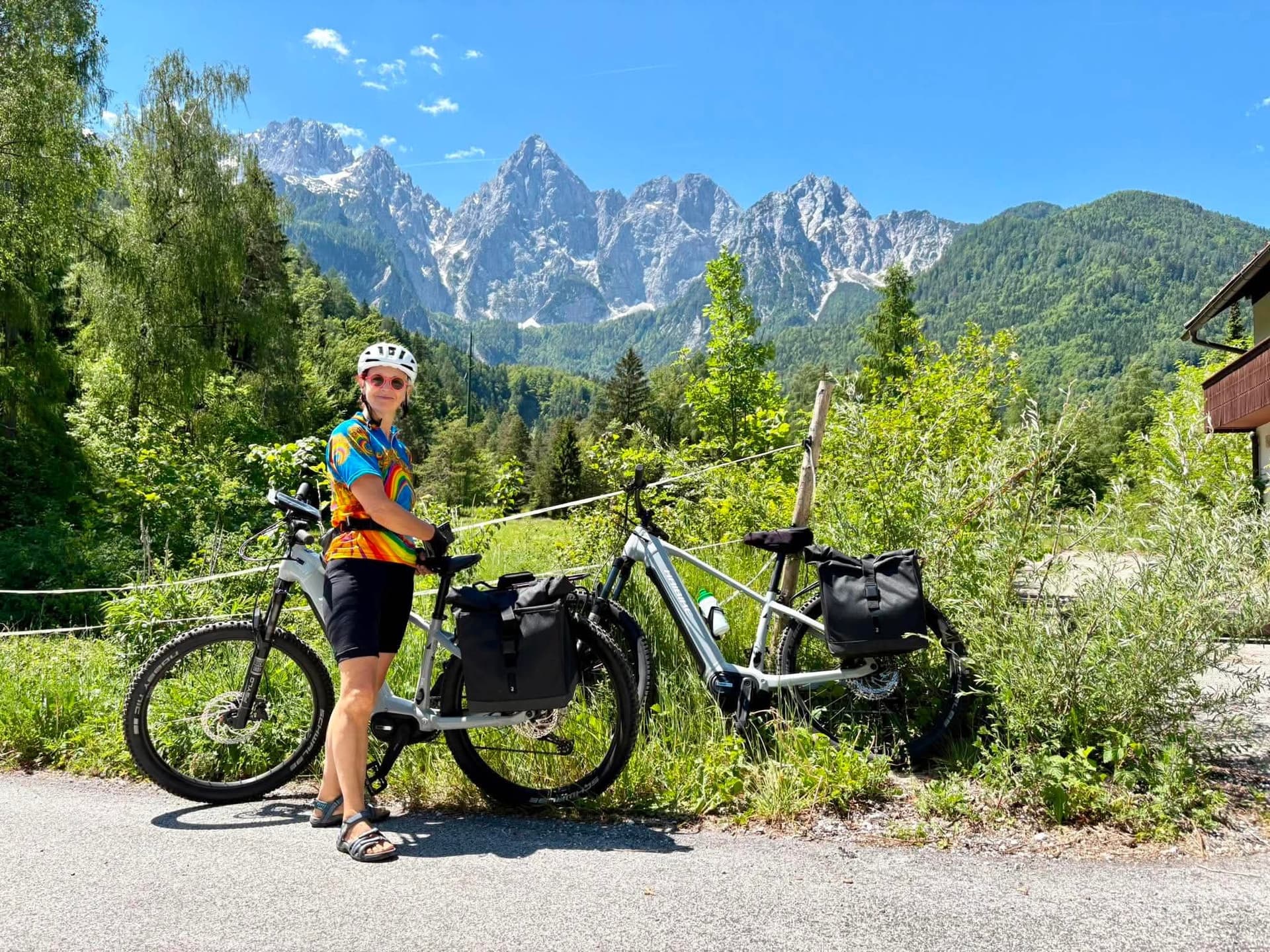 Cyclist with e-bikes and panniers standing below jagged mountain peaks